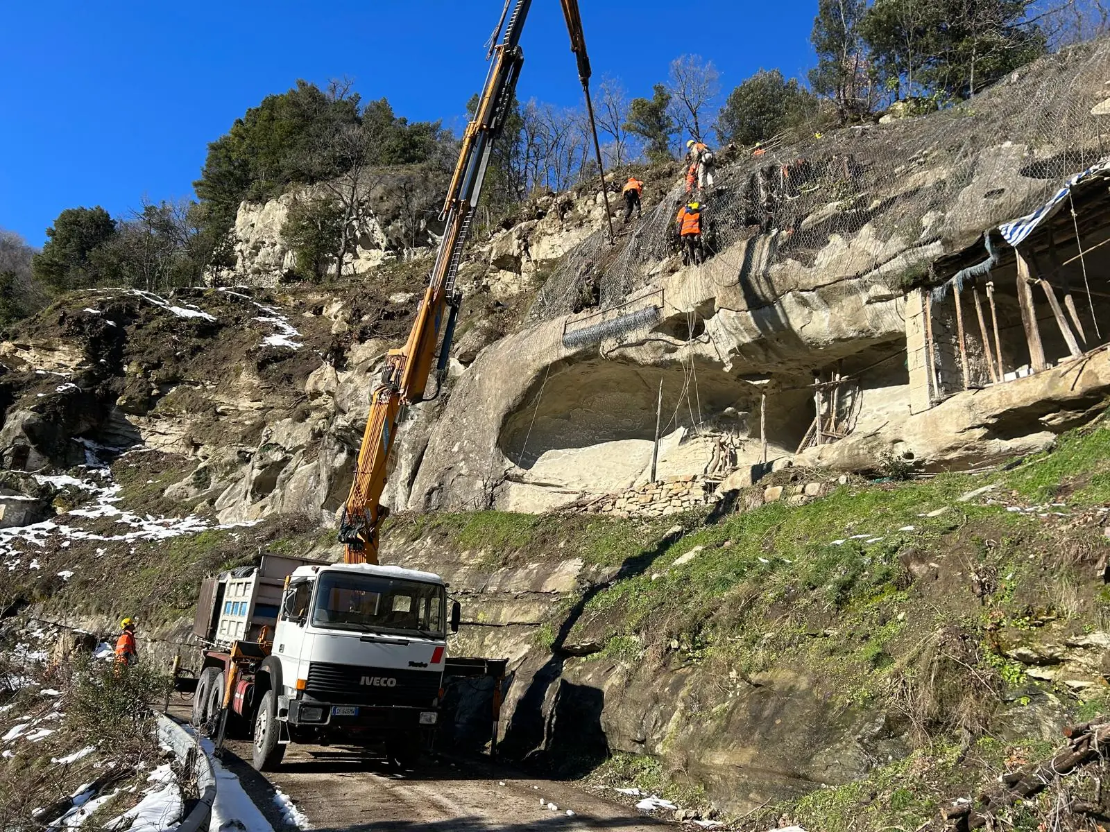 Autogru e operatori al lavoro su una parete rocciosa sopra la strada