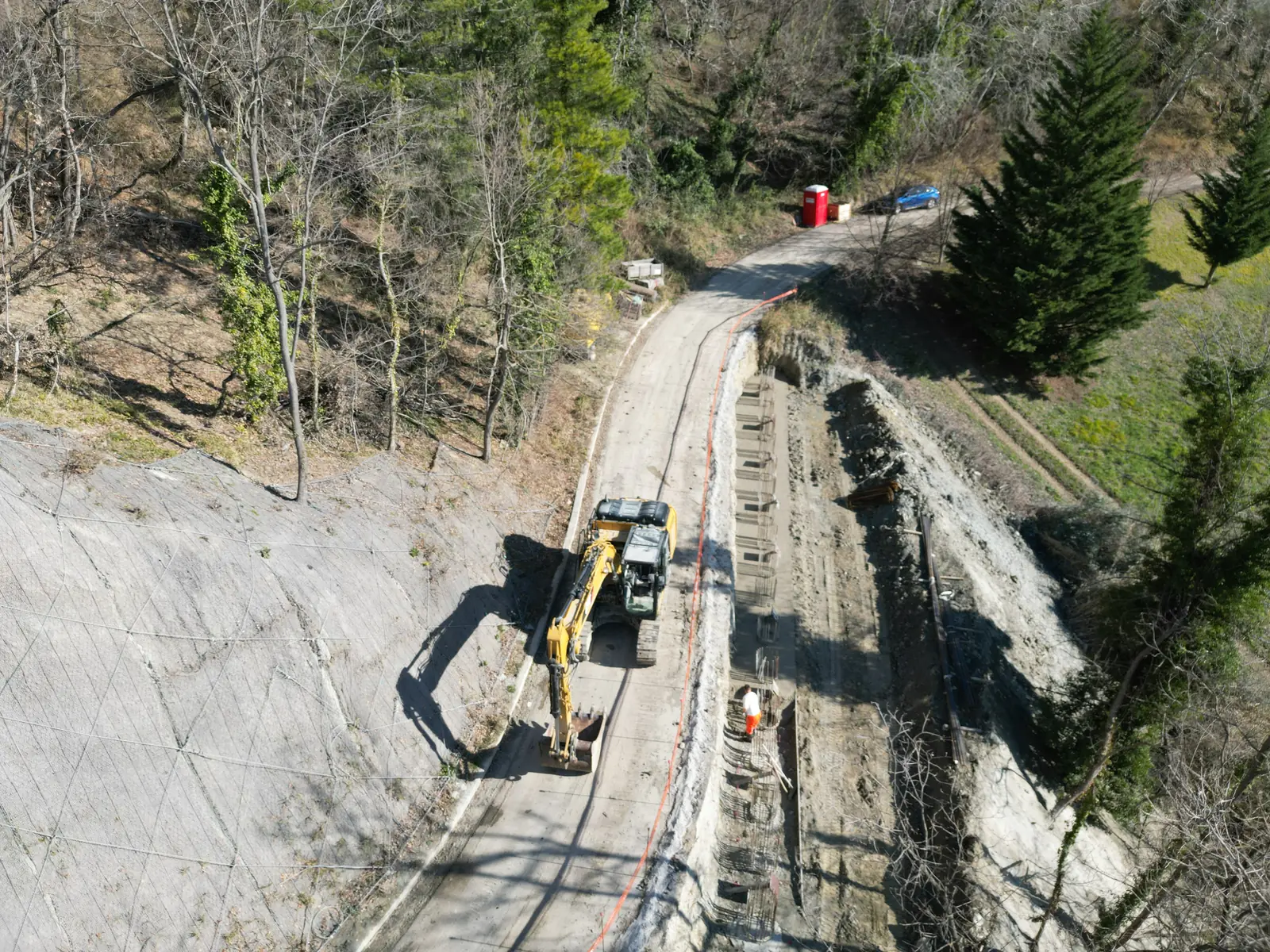Escavatore al lavoro sulla sede stradale al piede di una scarpata consolidata